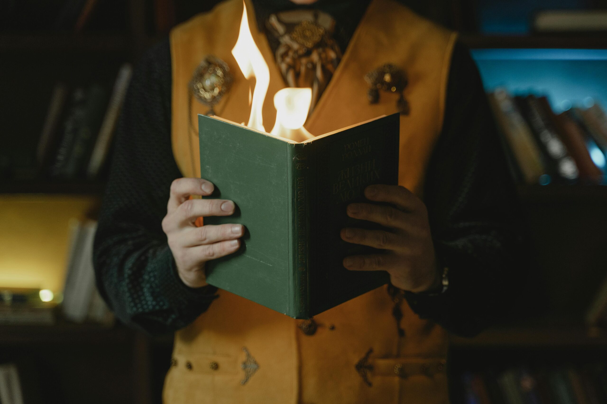 A magician holding a flaming book during a mystical performance indoors.